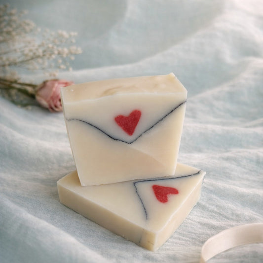 2 handmade soaps envelope shaped with red hart on an aqua linen and pink rose