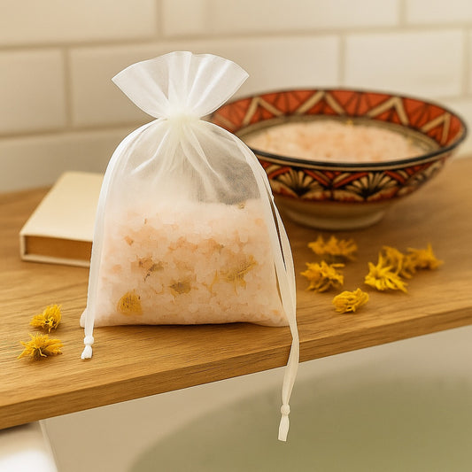 Organza drawstring bag filled with pink Himalayan salt and dried calendula petals, resting on a wooden bath ledge near a patterned bowl.