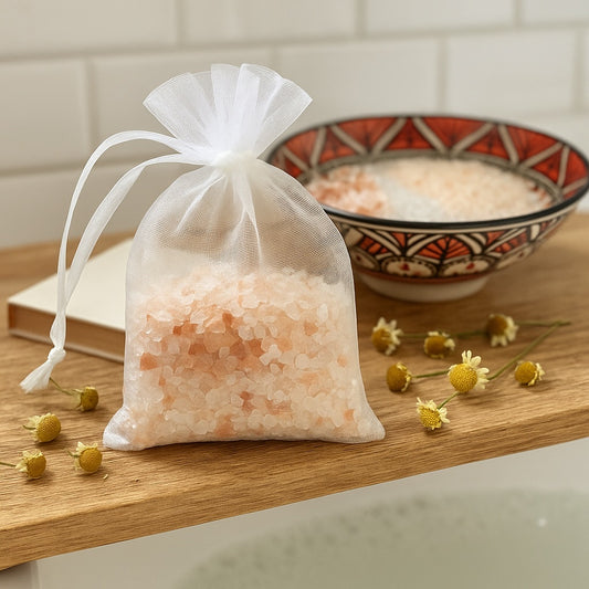 White sheer bag containing Himalayan pink salt and chamomile flowers, displayed on a wooden surface beside loose chamomile buds.