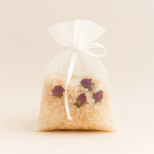 Transparent organza bag filled with pink Himalayan salt and rose buds, tied with a bow.