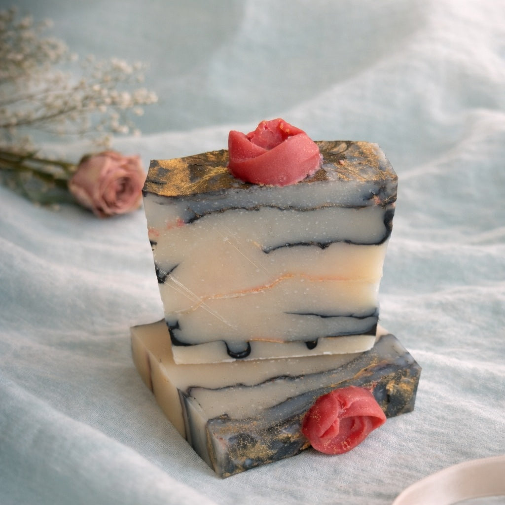 2 handmade marbled soaps with rose on top on a aqua linen and pink rose