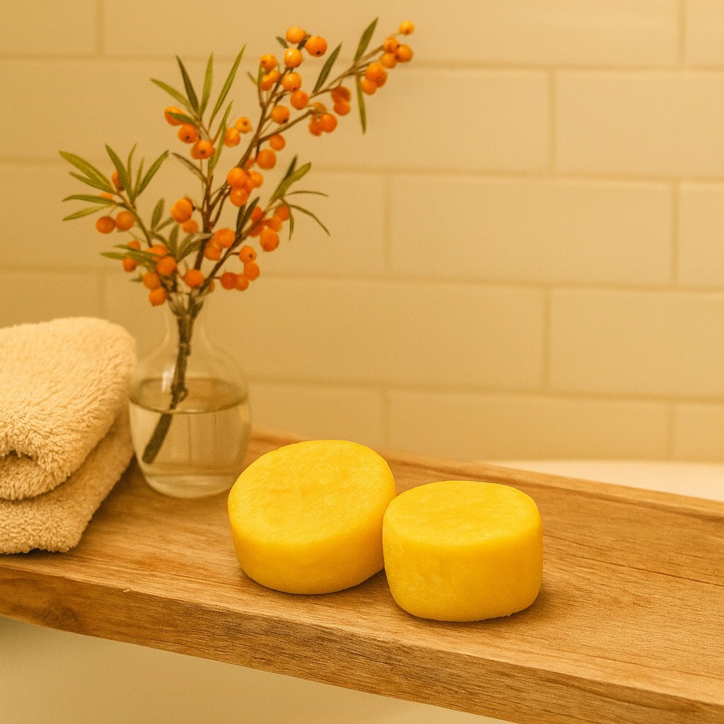 Handmade Seabuckthorn Grapefruit Shampoo Bars from Terra’s Touch displayed on a rustic wooden bath shelf above a bathtub, styled with a folded beige towel and a glass vase holding seabuckthorn berries in a warm country chic setting.
