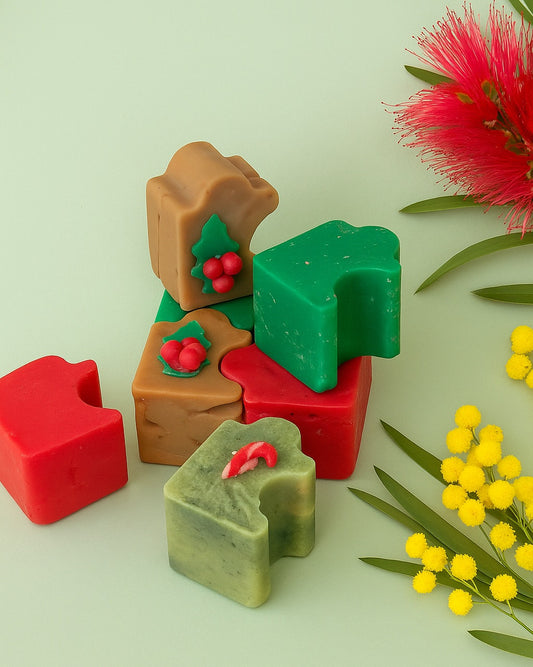 Christmas-themed puzzle soaps arranged playfully on a festive background with red bottlebrush and yellow wattle flowers, captured in warm natural lighting and a country chic style.