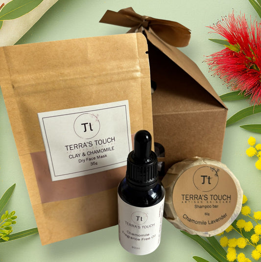 Pure Care Trio gift set from Terra’s Touch displayed on a soft green botanical background with wattle and bottlebrush. Includes a Clay & Chamomile dry face mask, Chamomile fragrance-free face oil, and Chamomile Lavender shampoo bar in a kraft gift box tied with a ribbon.