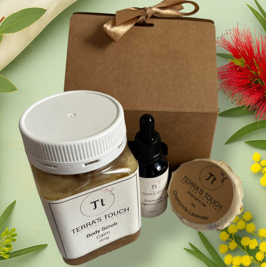 Renew & Nourish Set from Terra’s Touch displayed on a soft green botanical background with wattle and bottlebrush. Includes a Calm body scrub, Chamomile fragrance-free face oil, and Chamomile Lavender shampoo bar presented beside a kraft gift box tied with a satin ribbon.