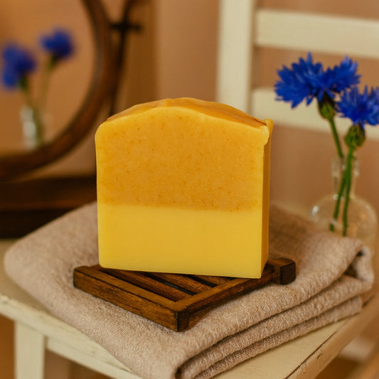 turmeric infused soap on a wooden sap saver and folded towel with cornflowers in a vase
