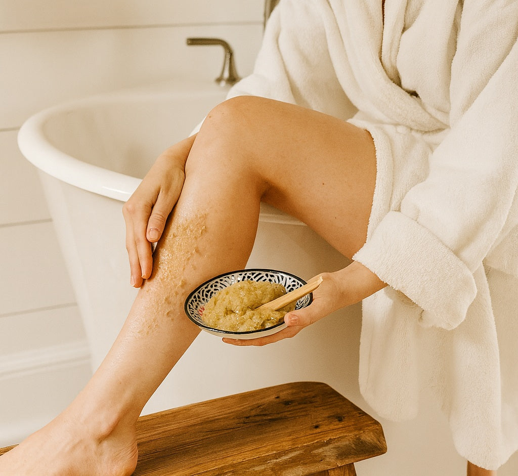 woman in white bathrobe using the emulsified body scrub on her leg